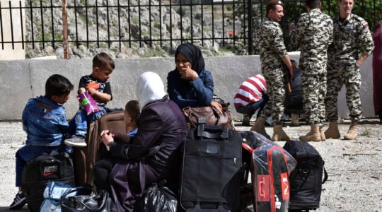 Displaced people who fled the Syrian war sit on their belongings near the Lebanese-Syrian border as they prepare to return to their village of Beit Jinn in Syria, while Lebanese General Security soldiers stand guard, in the southern village of Shebaa, Lebanon, Wednesday, April, 18, 2018. Hundreds of refugees are headed back to Syria in what they say is a voluntary decision to return to homes in the war-torn country. (AP Photo/Ziad Choufi)